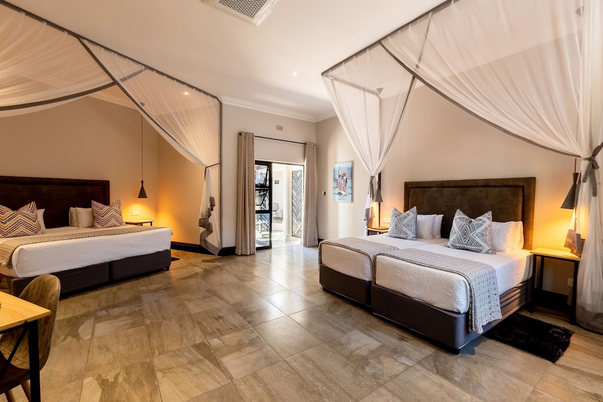 A hotel room with two beds, a dining area, and a view of the outside.