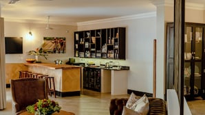 A modern living room with a brown leather sofa, a wooden coffee table with flowers, and a television mounted on the wall. - Nkosi Guest Lodge (Victoria Falls)