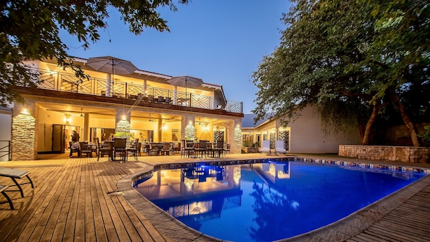 A poolside area with a wooden deck, outdoor seating, and a building with a balcony. - Nkosi Guest Lodge (Victoria Falls)