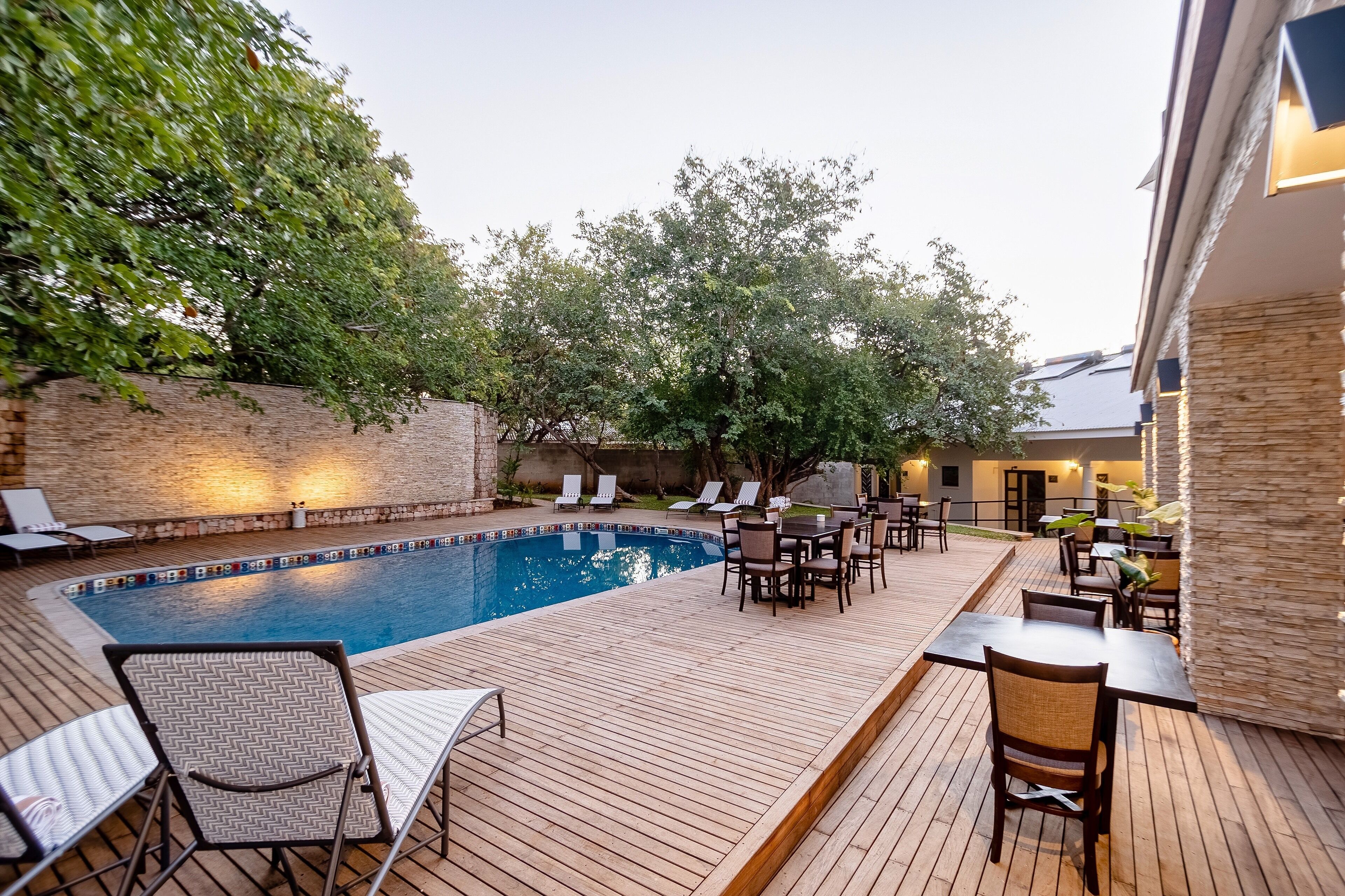Un espace aménagé au bord de la piscine, avec une terrasse en bois, des chaises longues et une table entourée de chaises.