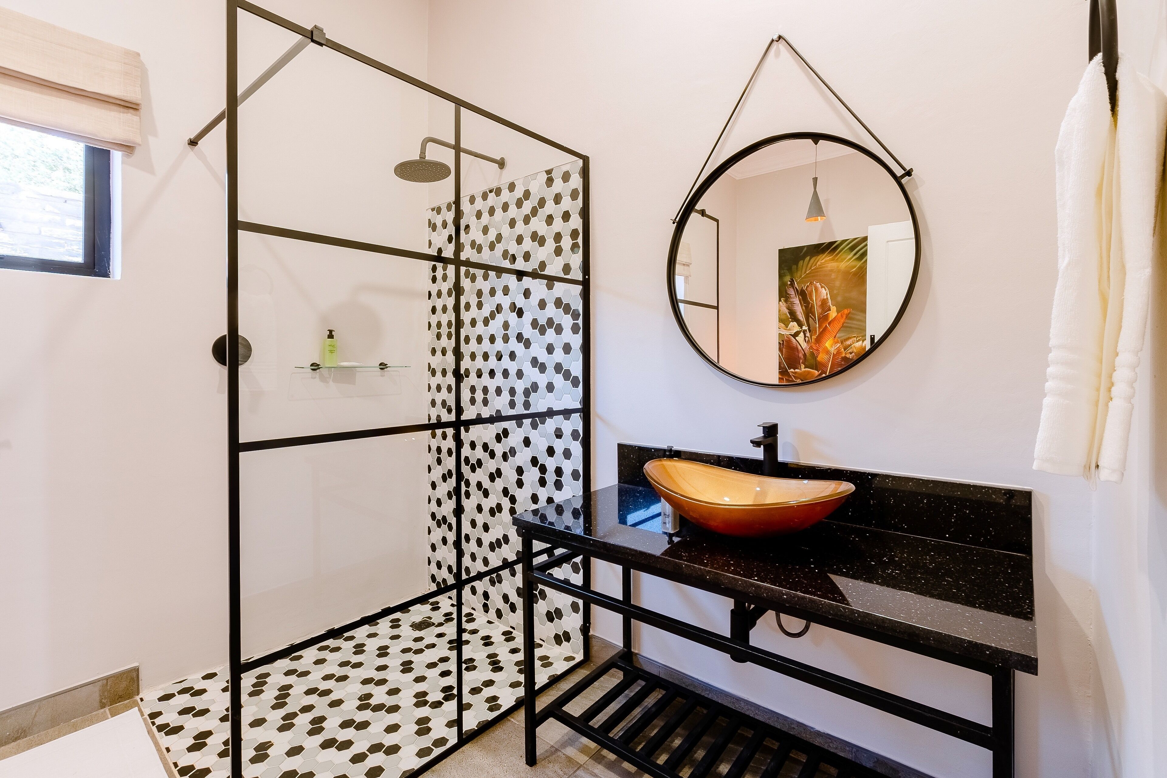 A modern bathroom with a glass shower enclosure, a round mirror, and a black countertop with a vessel sink.