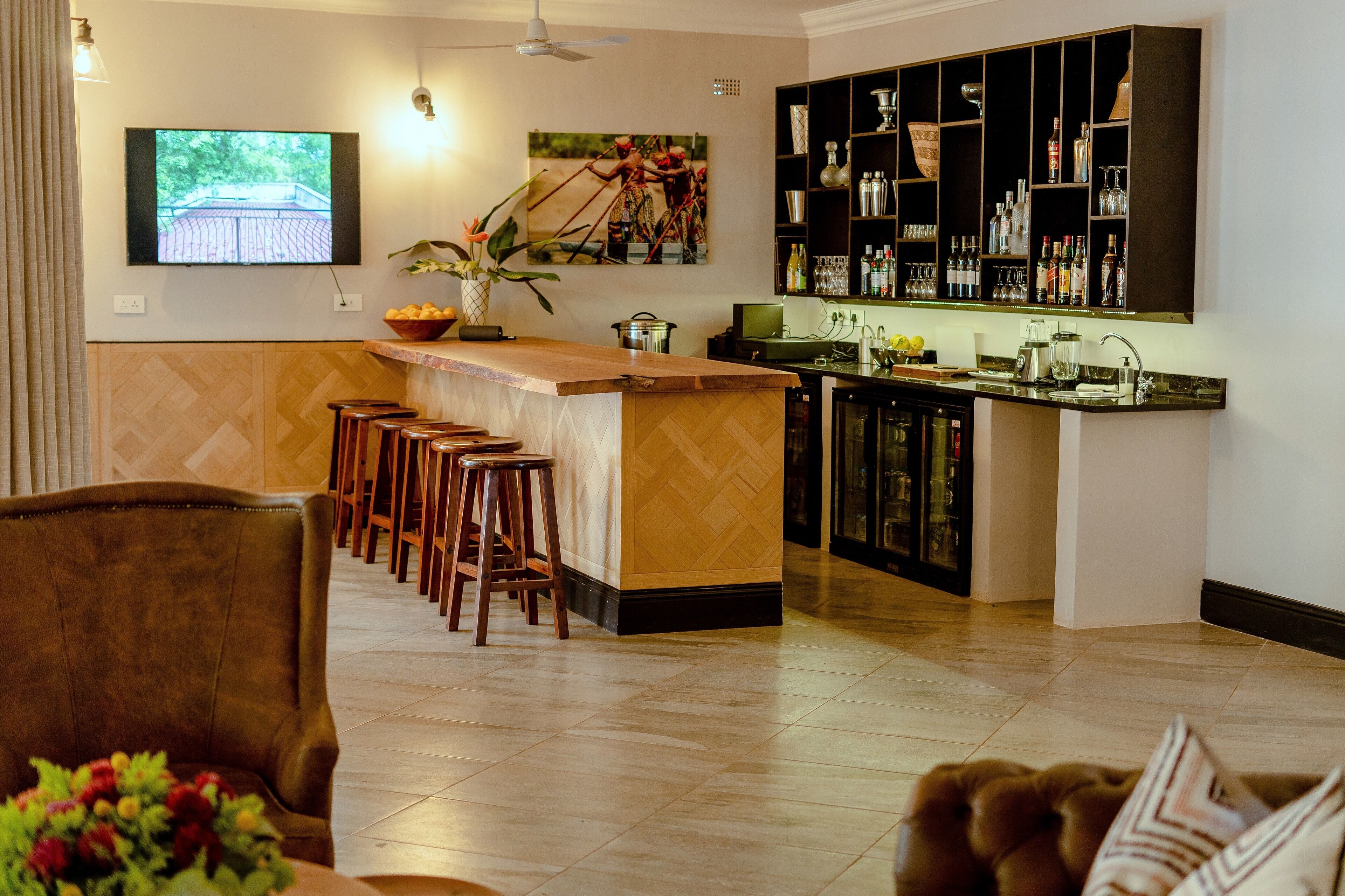 A modern kitchen with a bar area, wooden stools, and a television mounted on the wall.