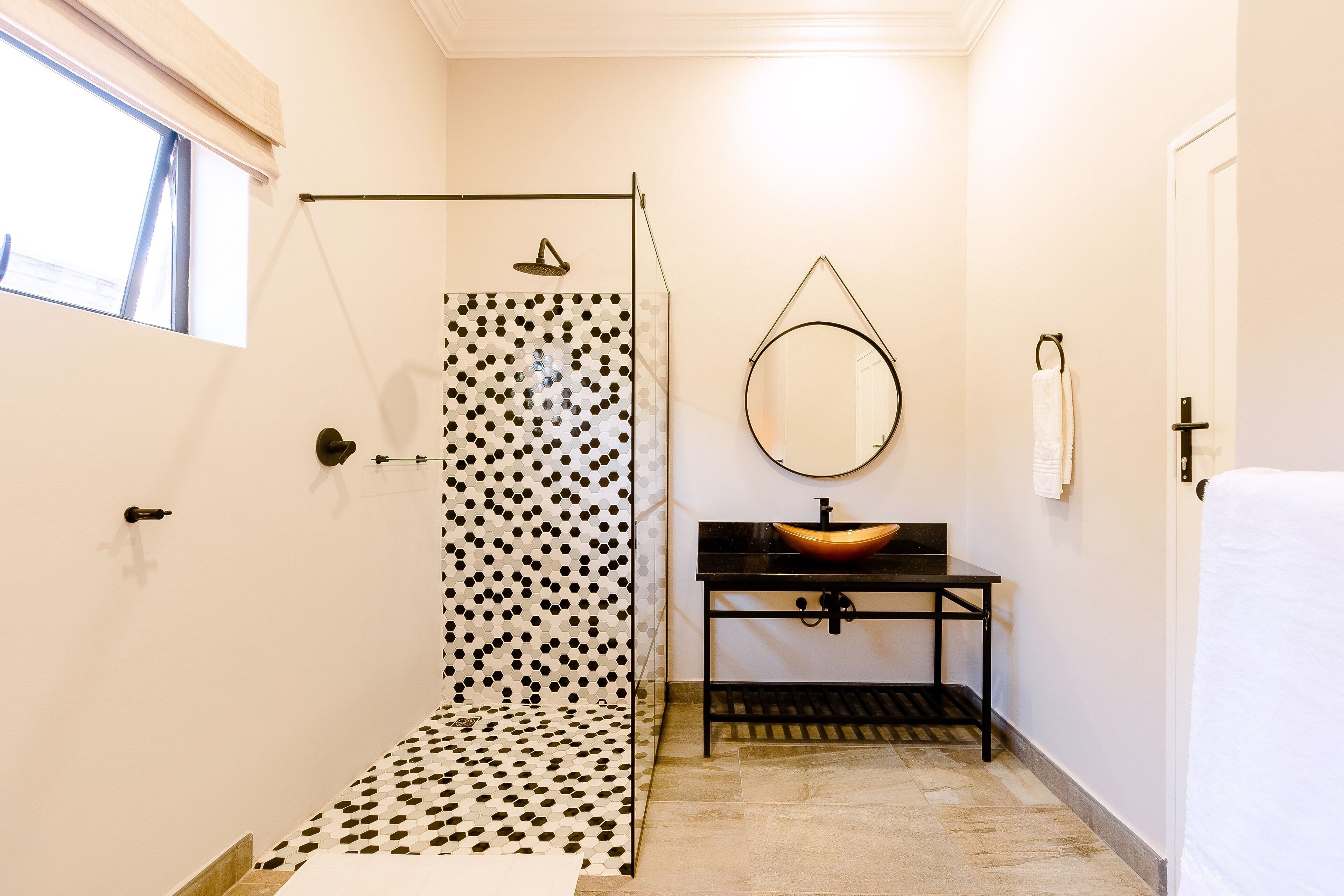 A bathroom with a shower, a sink with a round mirror, and a towel rack.