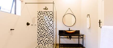 A bathroom with a shower, a sink with a round mirror, and a towel rack.