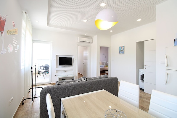 Relax in a spacious living area with a dining table, comfortable sofa, and mounted TV for entertainment.