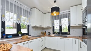 A modern kitchen with white cabinets, a wooden countertop, a black pendant light, and a window with lace curtains.