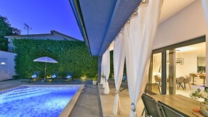 A swimming pool with lounge chairs, a covered patio area, and a dining space with tables and chairs.