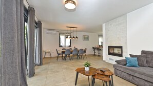 A modern living room with a sofa, a coffee table, and a fireplace. There is a dining area with a table and chairs in the background.