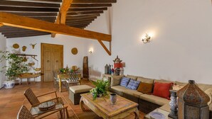 Amplio salón con techo alto, vigas de madera, un conjunto de sofás, una mesa de comedor y varios objetos decorativos.