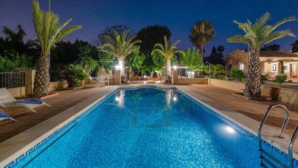 Una piscina con un diseño geométrico de azulejos, rodeada de palmeras y un cielo nocturno.