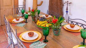 Una mesa de madera con platos, tazones y vasos verdes, rodeada de sillas.