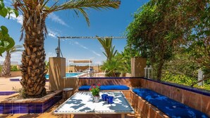 Zona junto a la piscina con una mesa, cojines azules y vistas a la piscina.