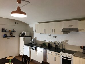 A compact kitchen with a dishwasher, stove, and microwave. There are cabinets, a sink, and a hanging light fixture.