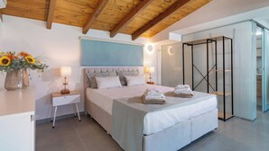 A bedroom with a wooden ceiling, a bed with a blue headboard, bedside lamps, a nightstand, and a vase of flowers.