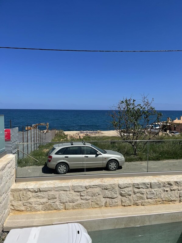 A coastal road with a parked car, a stone wall, and a clear view of the sea. - OceanEye Suites - Aura (Panormo)