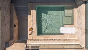 A spa area with a large rectangular hot tub, a stone wall, and a small seating area with cushions.