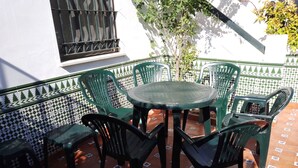 Een terras met een ronde tafel en zes groene stoelen, omringd door geplakte vloertegels.