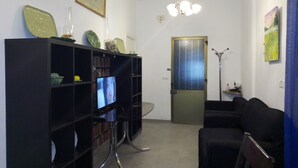 Een woonkamer met een zwarte bank, een zwarte boekenkast, een televisie en een deur.