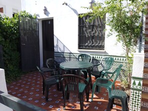 Une terrasse avec une table ronde et des chaises, un sol carrelé et une fenêtre ornée de barreaux décoratifs.