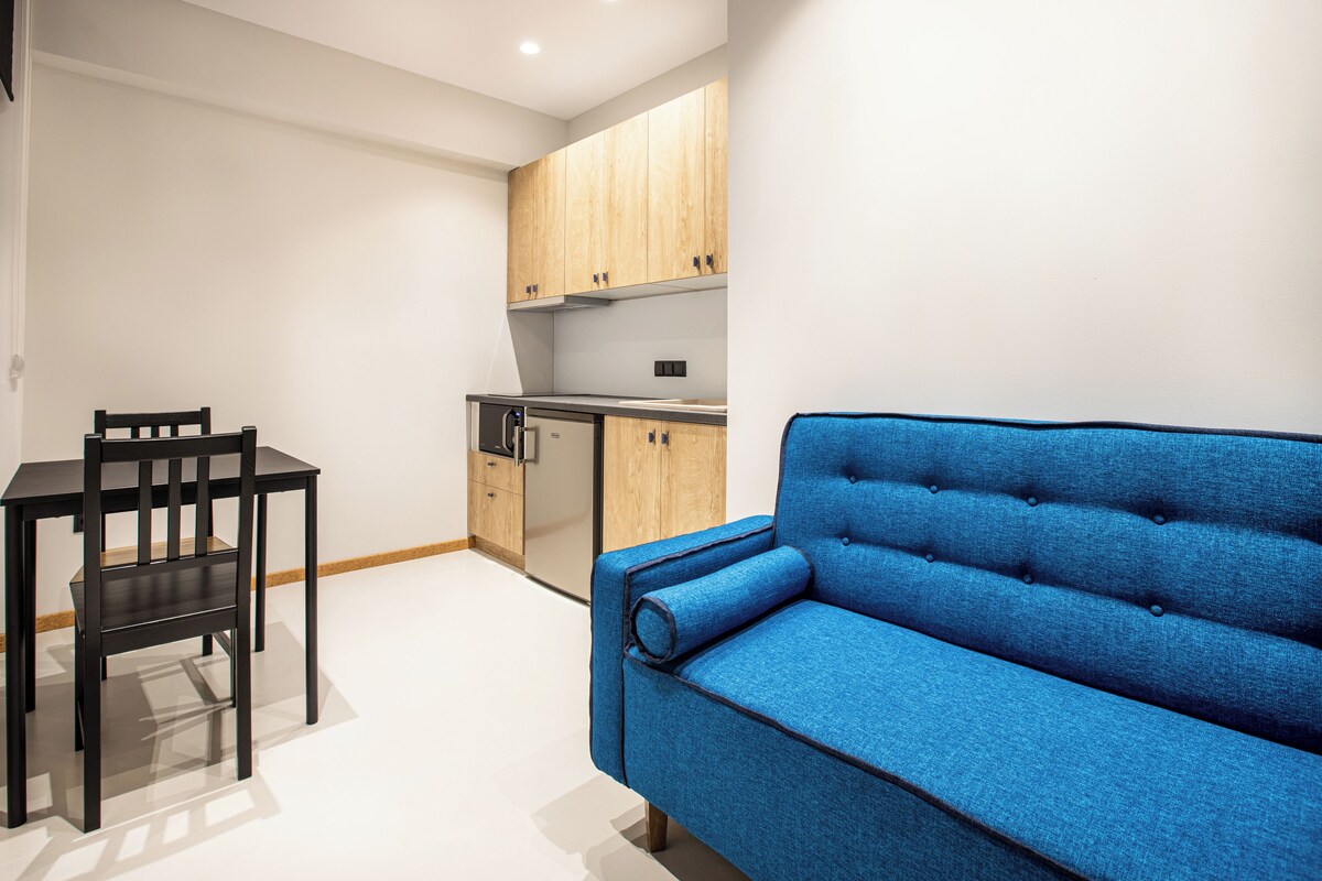 A compact living space with a kitchenette, a blue sofa, and a dining table with chairs.