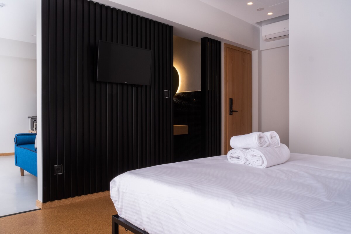 Una habitación de hotel moderna con una cama grande, un televisor de pantalla plana en la pared y un sofá azul en la esquina.