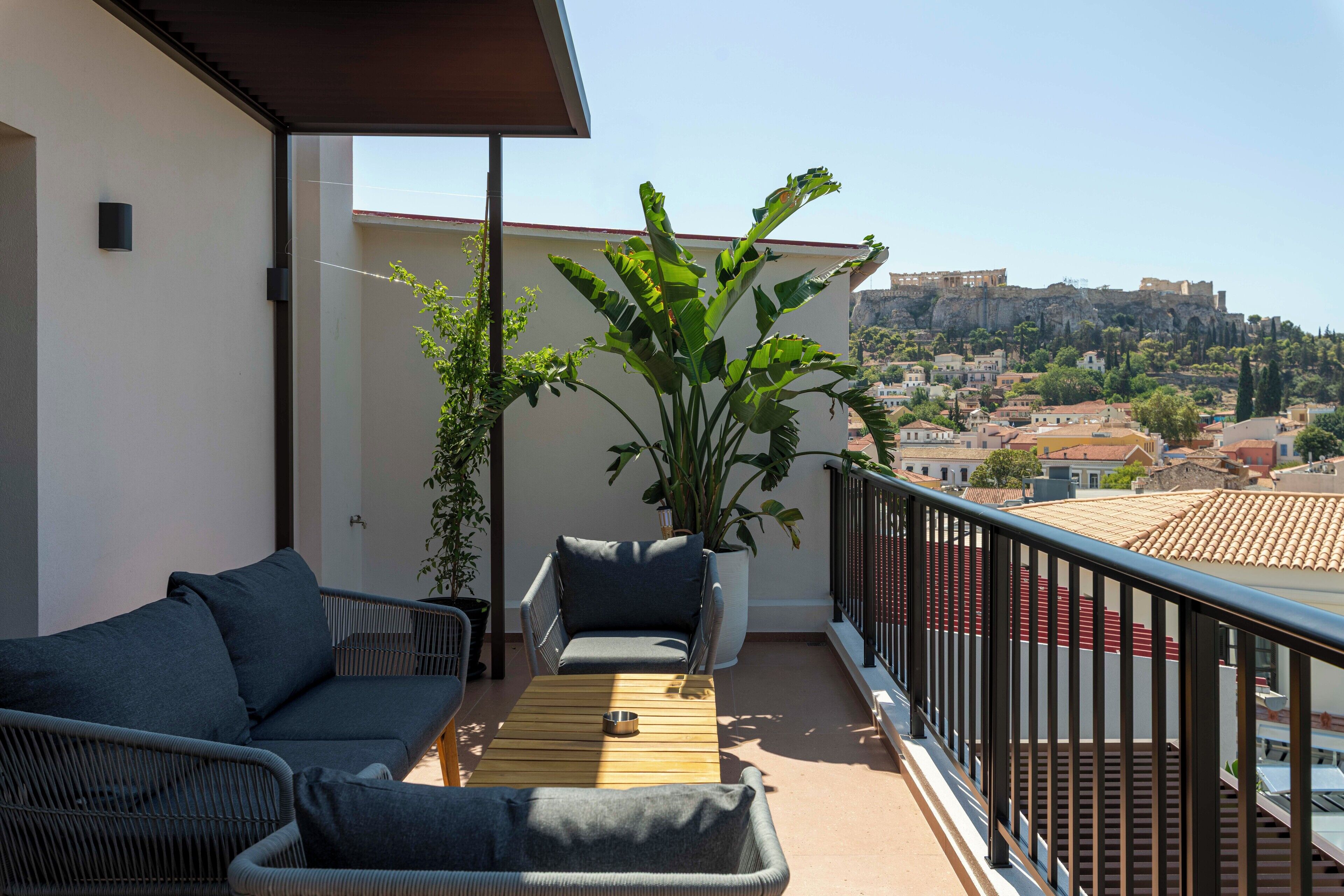 A balcony with wicker furniture, a potted plant, and a view of a historic cityscape.