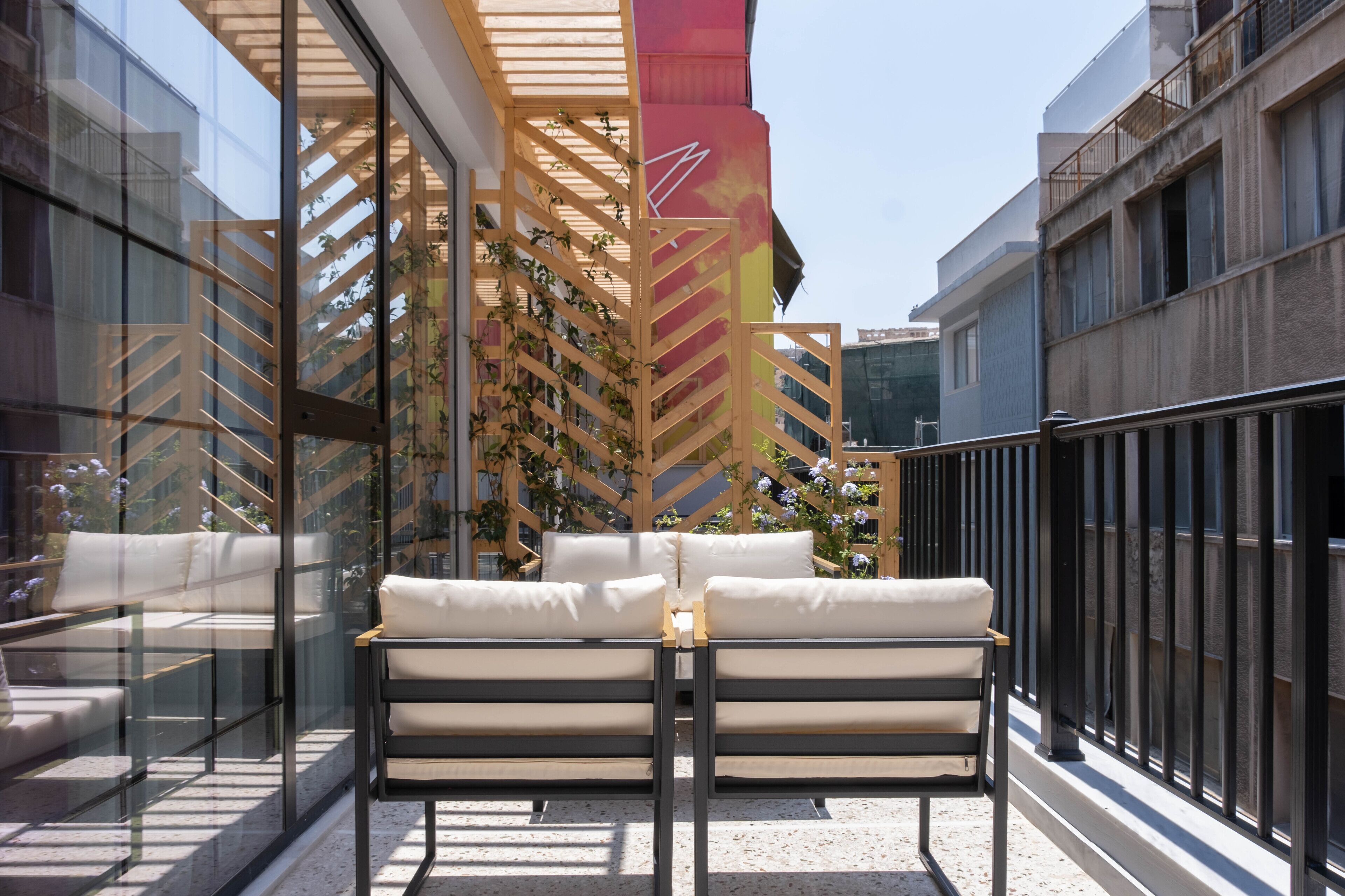 Zona relax esterna moderna con due poltrone bianche imbottite e un tavolo in vetro, circondata da una pergola in legno con piante rampicanti.