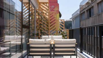 Zona relax esterna moderna con due poltrone bianche imbottite e un tavolo in vetro, circondata da una pergola in legno con piante rampicanti.