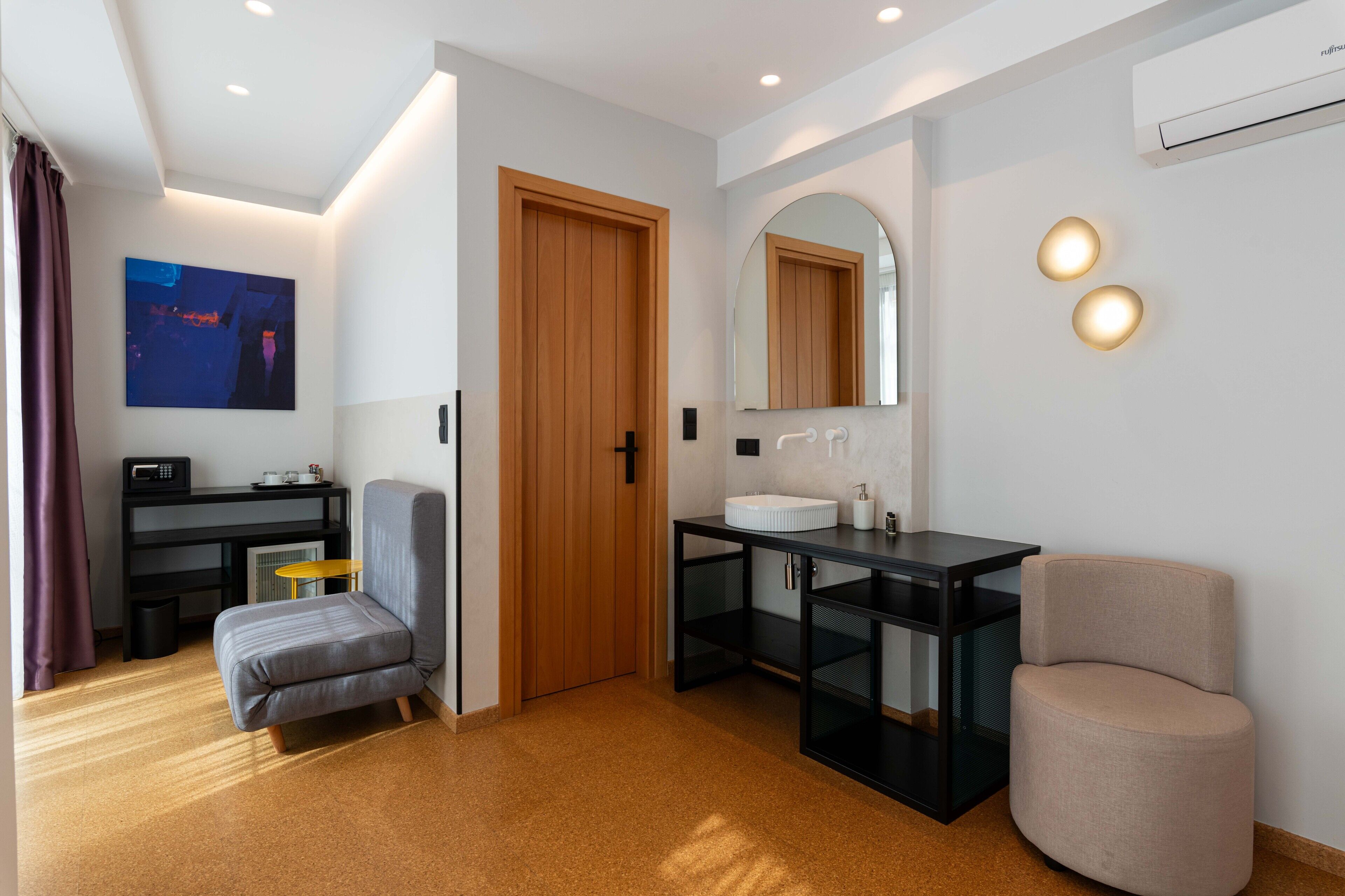 A modern bathroom with a wooden door, a large mirror, and a sink. There is a chair and a small table with a radio.