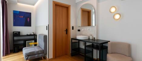 A modern bathroom with a wooden door, a large mirror, and a sink. There is a chair and a small table with a radio.