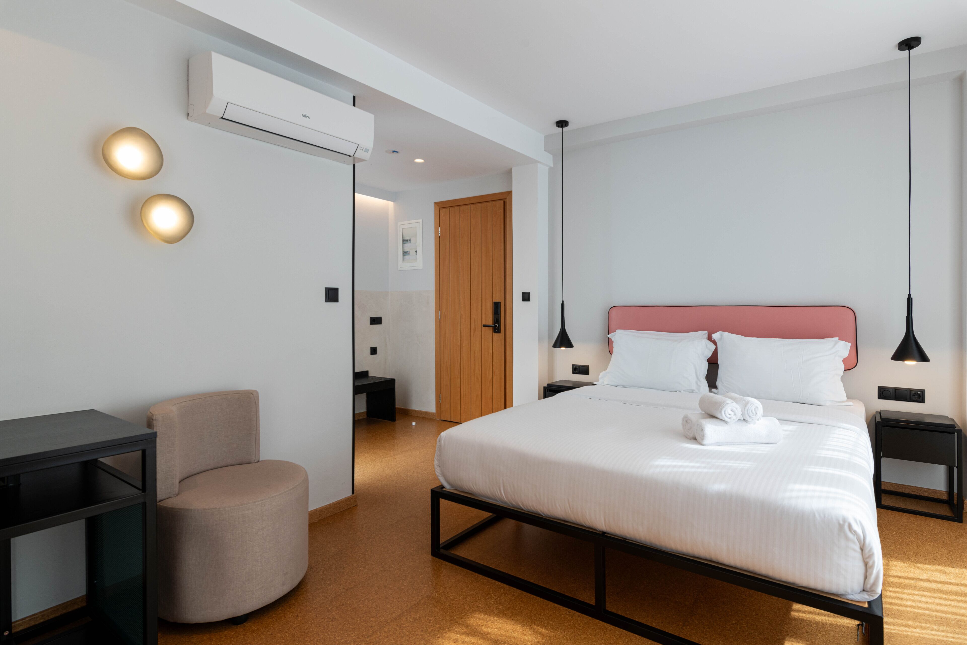A modern hotel room with a bed, bedside tables, a desk, a chair, and a wardrobe.