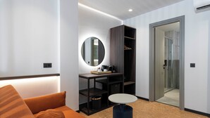 Una habitación de hotel moderna con un sofá, un espejo redondo, una mesita, un armario y una puerta de vidrio que da a una zona de ducha.