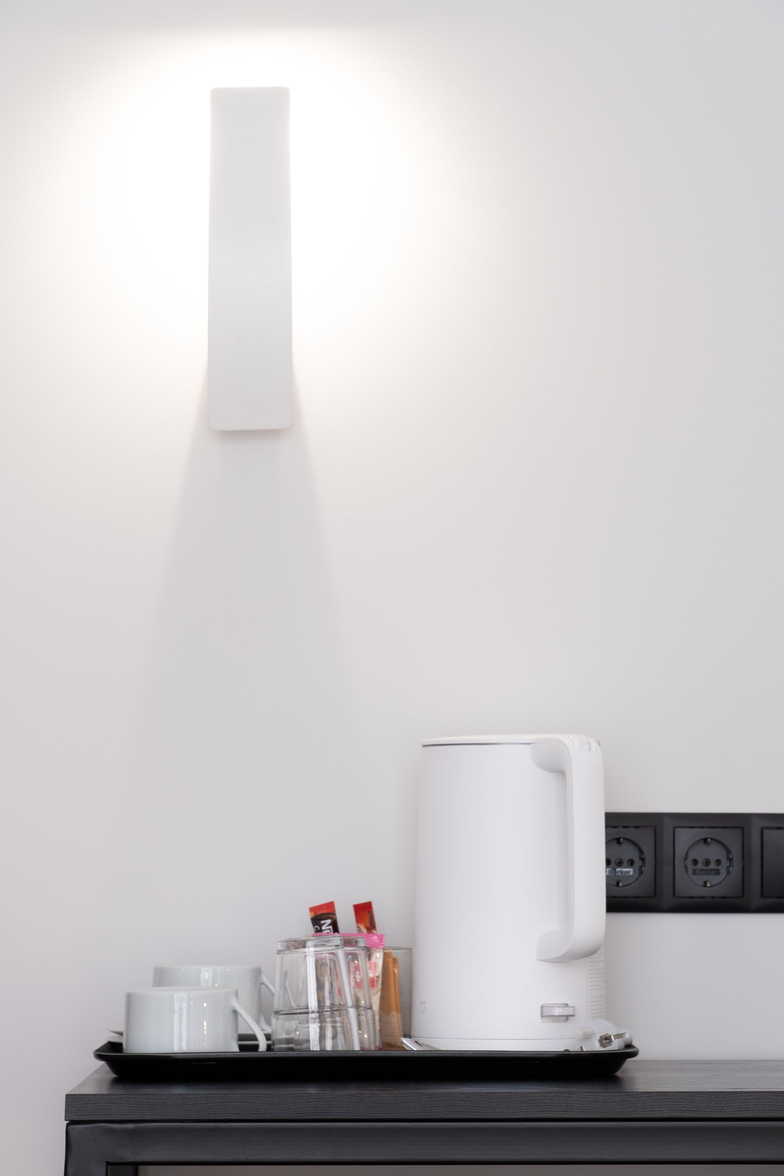 A modern kitchen with a white kettle on a tray, a coffee maker, and a glass of water on the counter.