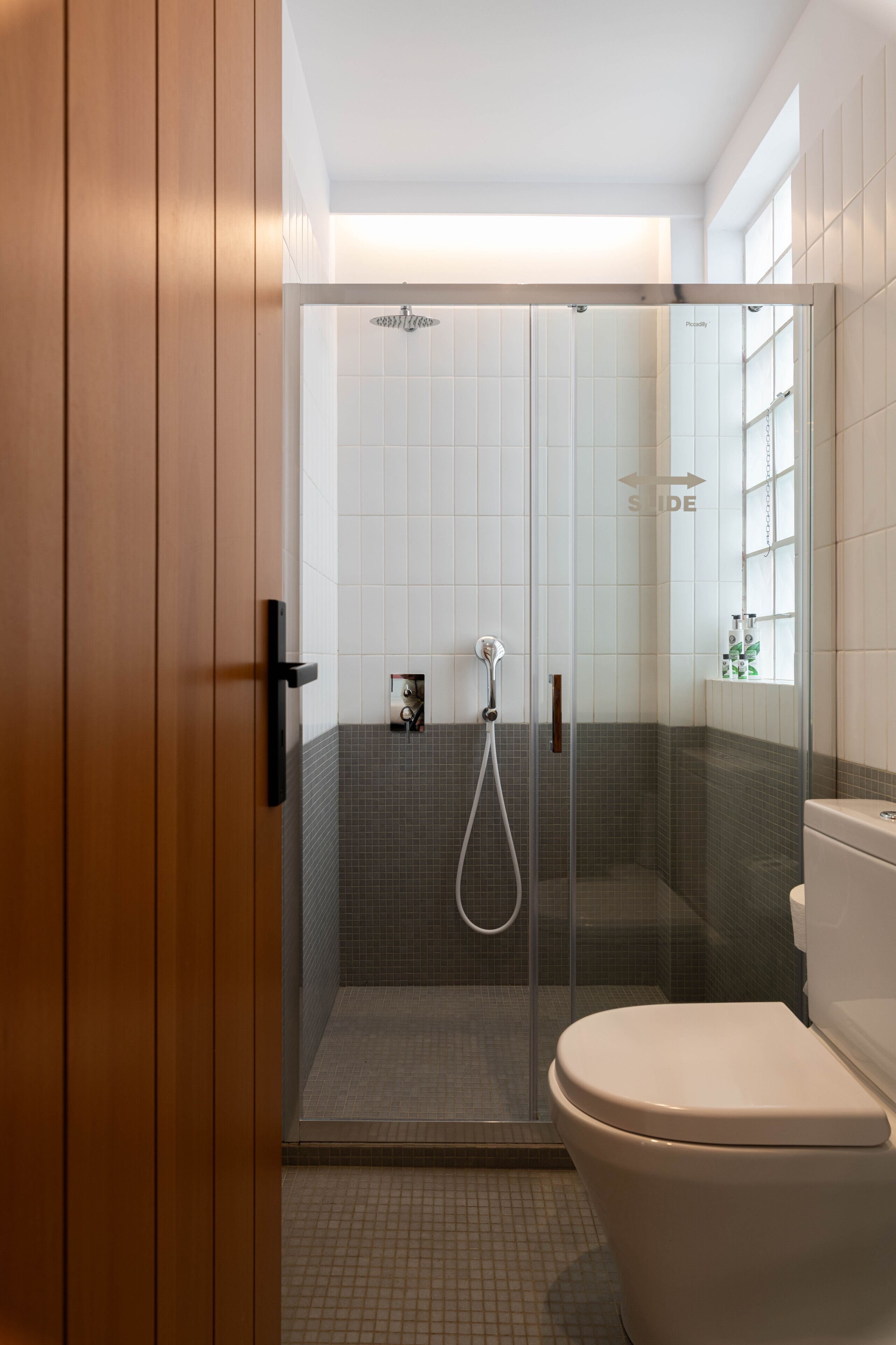 A modern bathroom with a glass-enclosed shower, a toilet, and a wooden door.