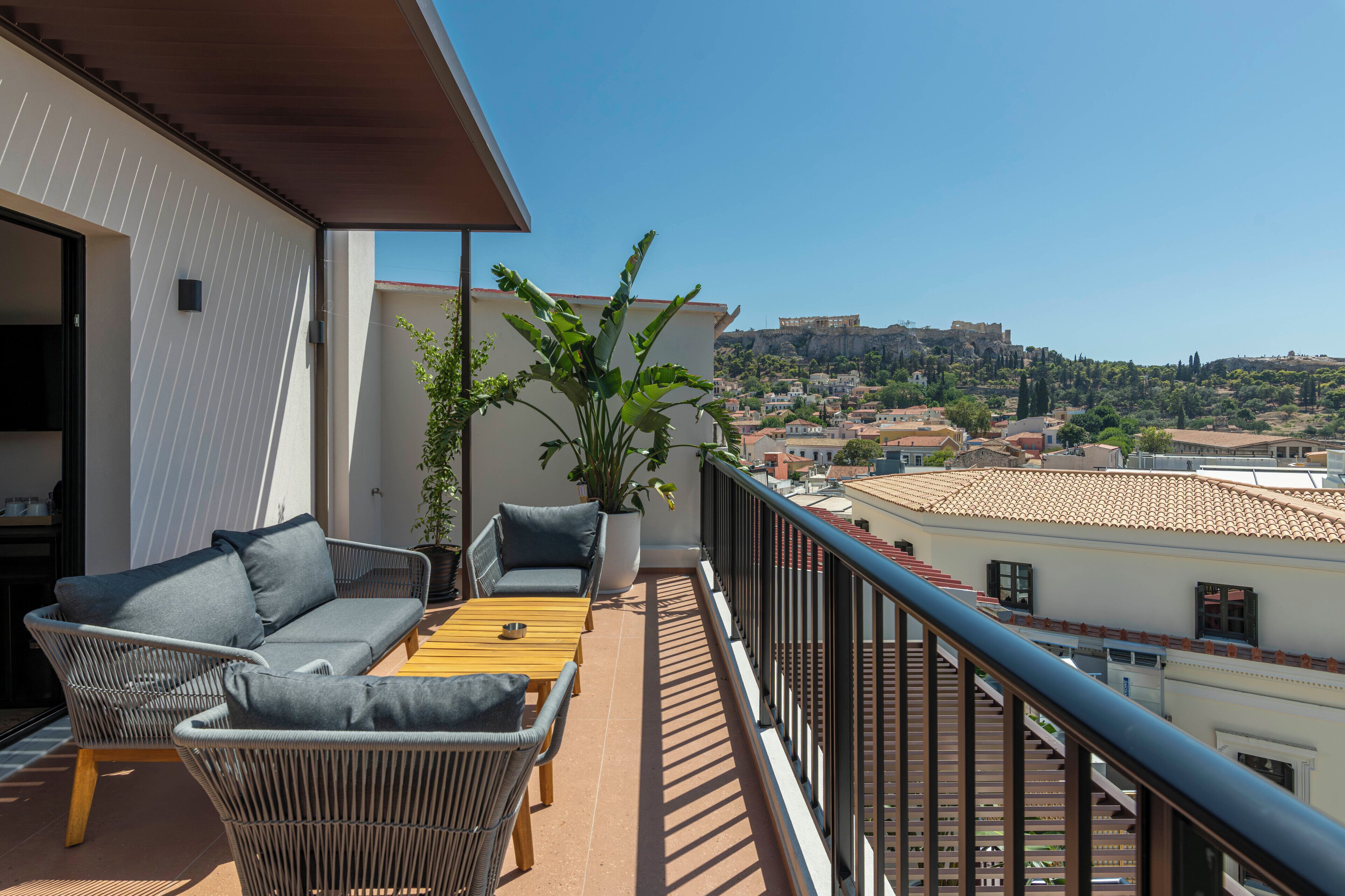 A balcony with wicker furniture, a potted plant, and a view of a historic cityscape.
