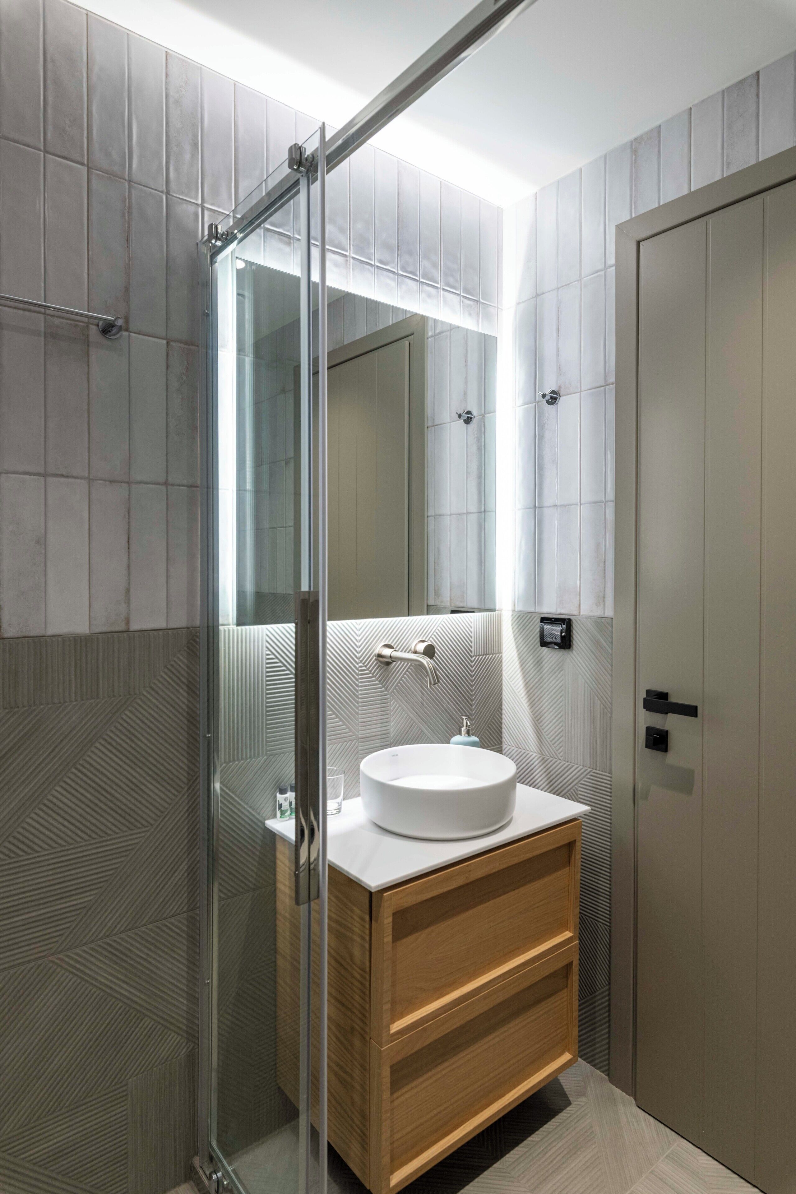 A modern bathroom with a glass shower enclosure, a wooden vanity, and a large mirror.