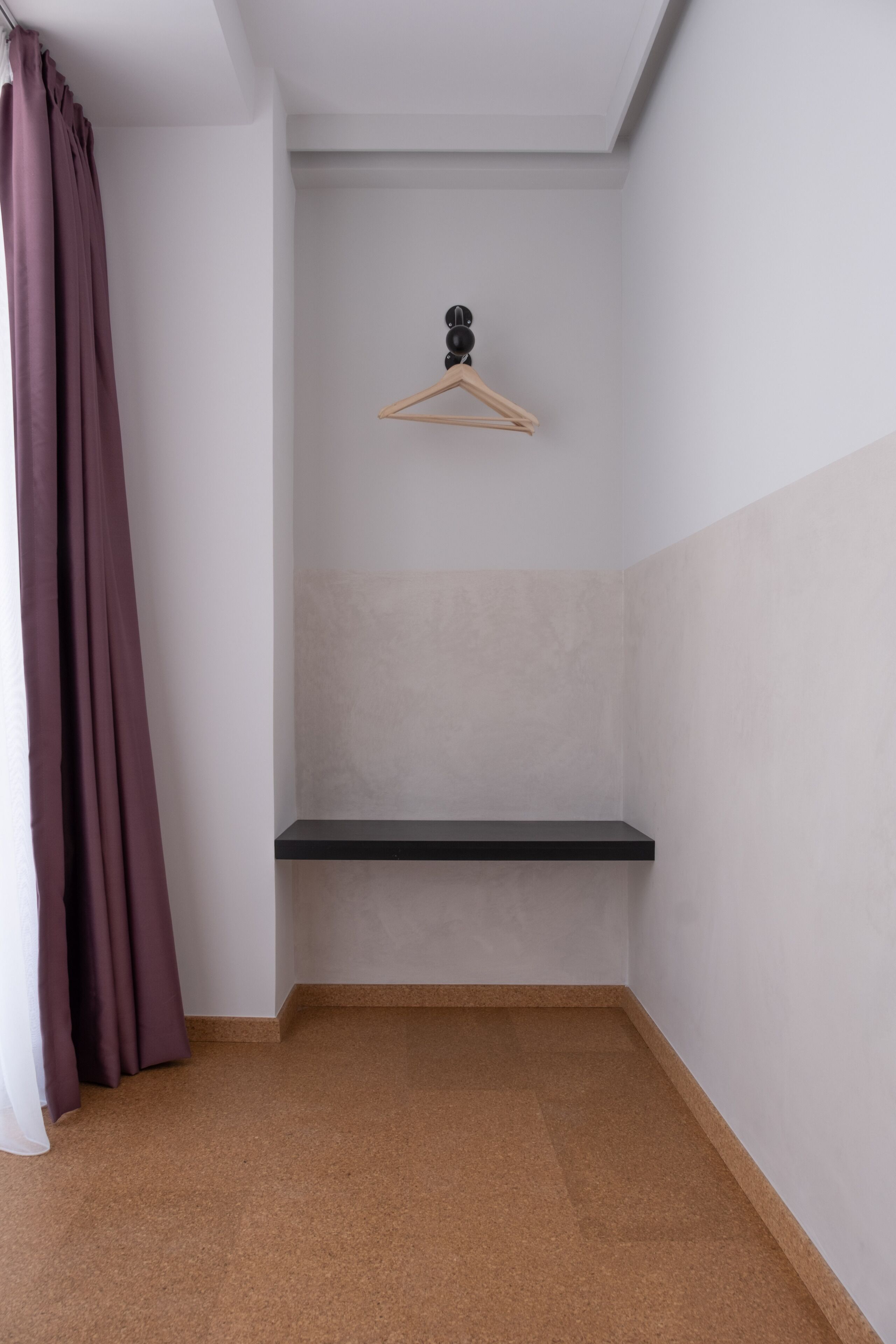 A corner room with a black shelf, a wooden hanger, and a curtain.