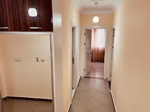 Un pasillo estrecho con un panel de madera a la izquierda y una puerta a la derecha que da a una habitación con cortina.