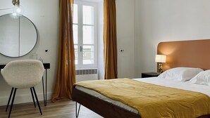 Ein Hotelzimmer mit Bett, Schreibtisch, Stuhl, Spiegel und einem fenster mit Vorhängen.