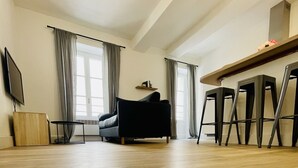 Ein geräumiger Wohnbereich mit einer Couch, einem Fernseher und einem Essbereich mit Hockstühlen.