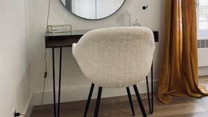 Ein Zimmer mit einem runden Spiegel, einem weißen Stuhl, einem Schreibtisch und einem Fenster mit Vorhängen.