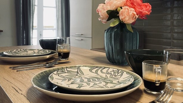 Eine moderne Küche mit einer Holzausziehtheke, einem Blumenstrauß und einer Esszeile mit Tellern, Gläsern und Besteck.