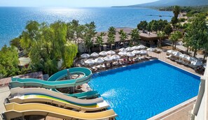 A swimming pool with a water slide, lounge chairs, umbrellas, and a view of the sea.