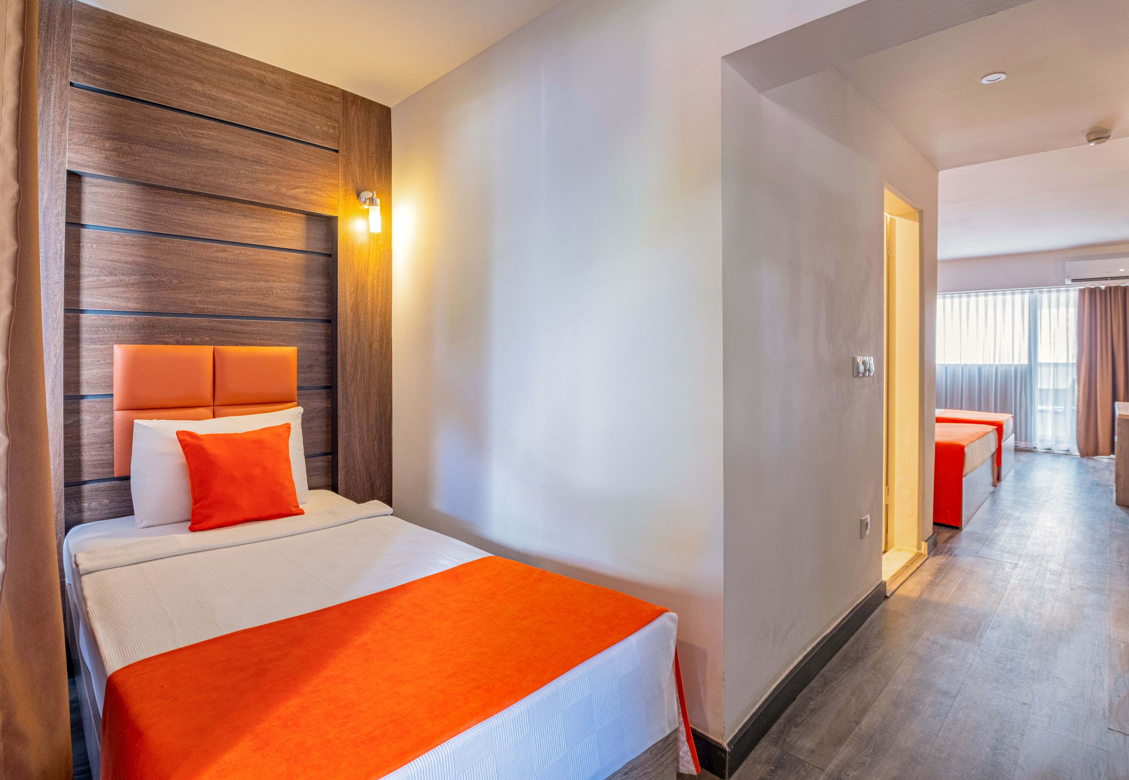 Quarto de hotel com cama, cabeceira de madeira, mesa de cabeceira e janela com cortinas.