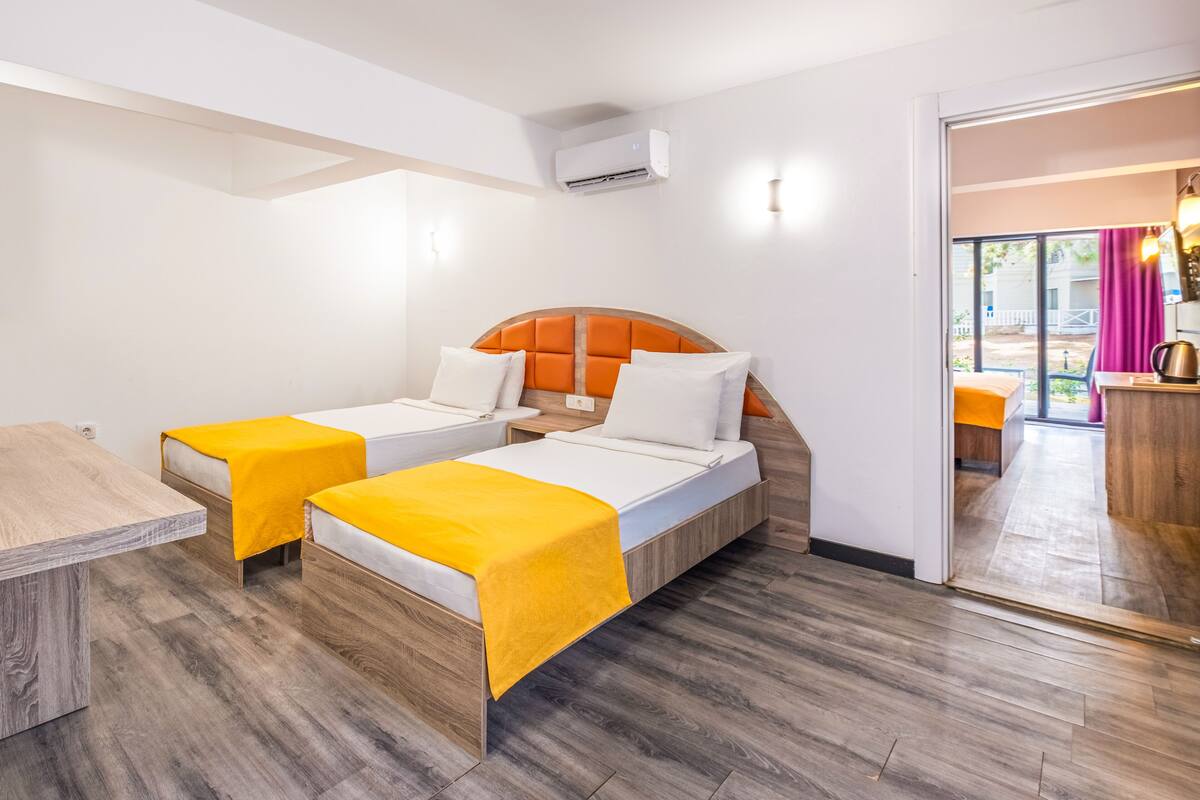 A hotel room with two single beds, a wooden desk, and a view of the outside.