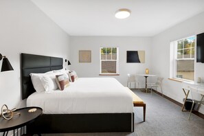 Ein Hotelzimmer mit einem großen Bett, einem kleinen Tisch, einem Sessel, einem Fernseher und einem Fenster mit Jalousien.