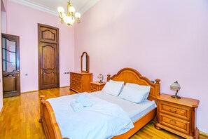 A bedroom with a wooden bed, a nightstand with a lamp, a dresser, and a door.