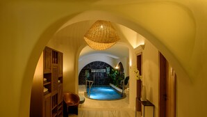 A hallway leading to a spa area with a stone fireplace, a hanging light fixture, and a bench. - Acro Blue Luxury Villas (Santorini)