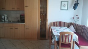 Une cuisine compacte avec des meubles en bois, un évier et une machine à café. On y trouve également un coin repas avec une table recouverte d’une nappe à motifs floraux et un canapé à rayures.