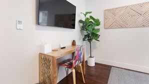 A modern room with a wooden desk, a flat-screen TV, a potted plant, and a geometric wall art piece.